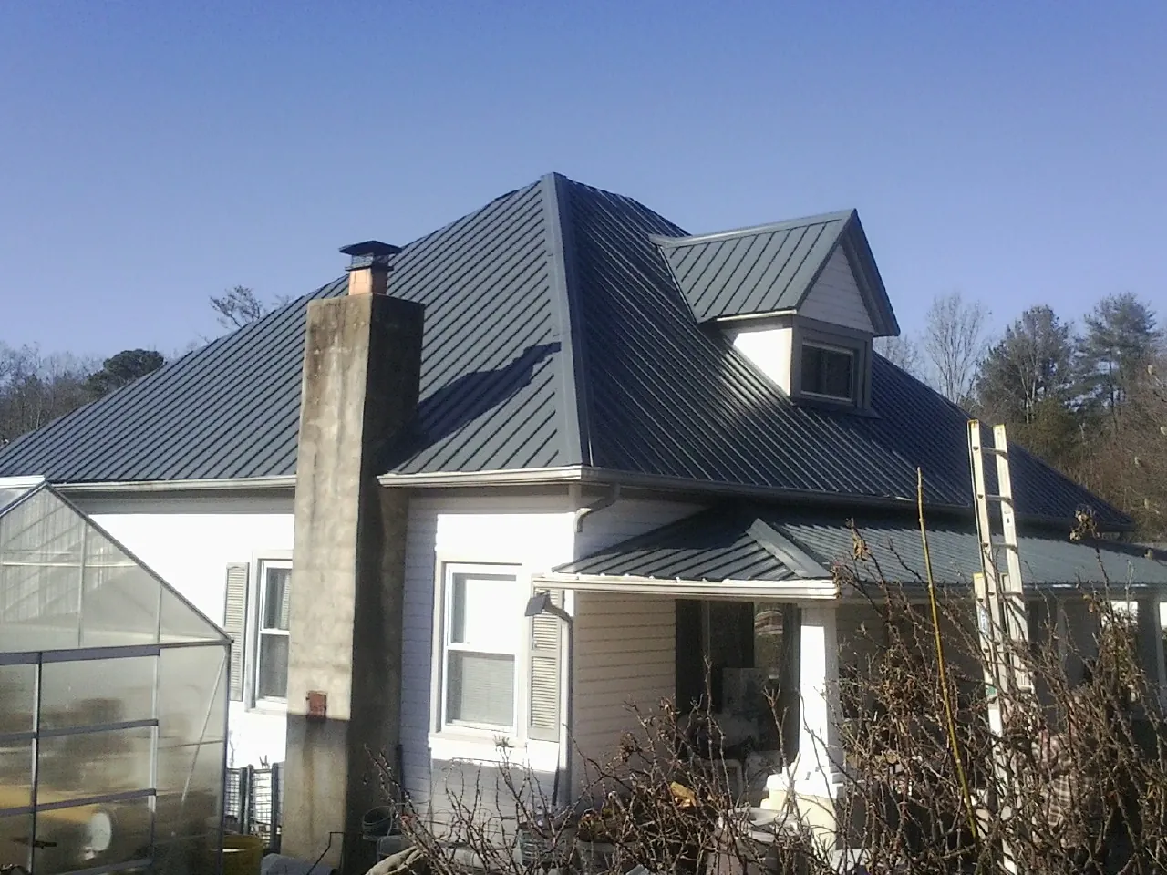 Dark blue standing seam metal roof on a white farmhouse with dormer — Slate & Tile Roof Repair by Roofing Brothers in Glasco