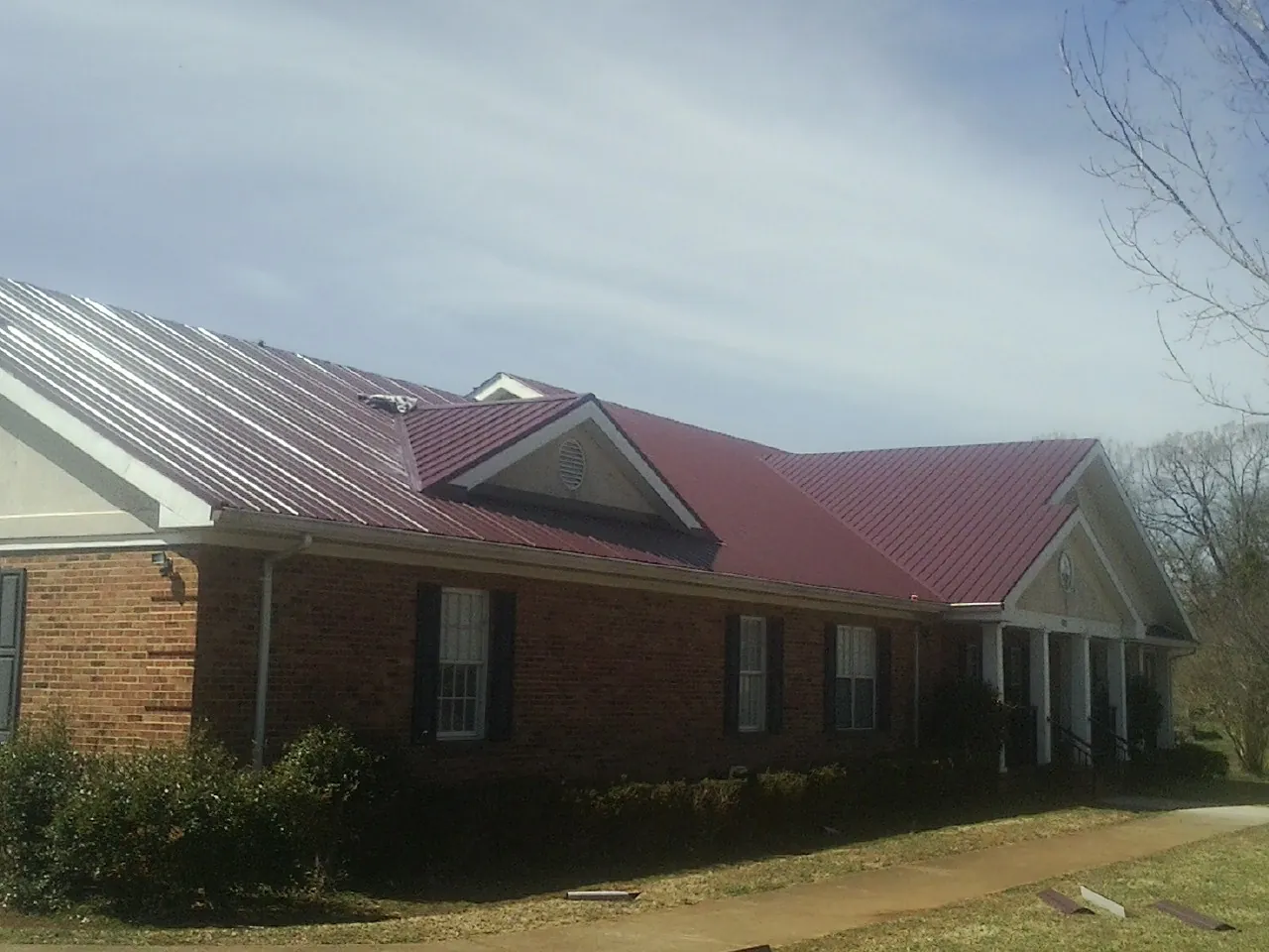 Red metal roof with gabled entries on a long brick building, from a Hail Damage Roof Repair job in Glasco
