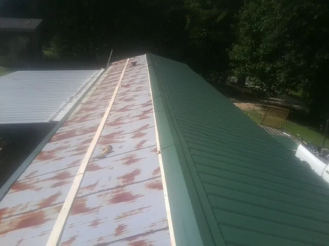 Old rusted panels beside newly installed green metal roofing — Wind Damage Roof Repair by Roofing Brothers in Glasco