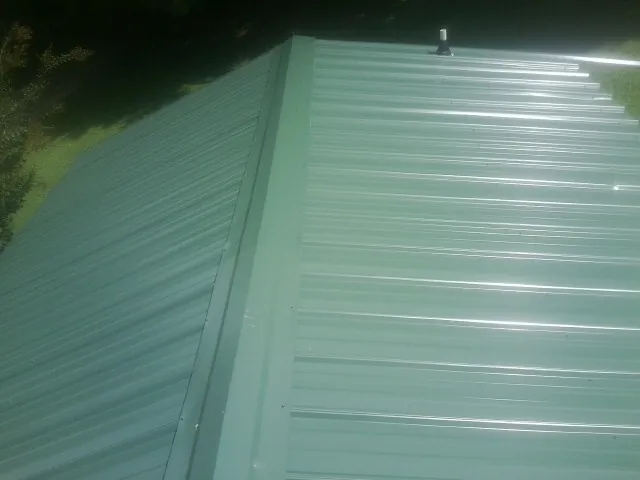 New green metal panels meeting at the ridge of a roof — Flat Roof Repair work by our crew in Glasco