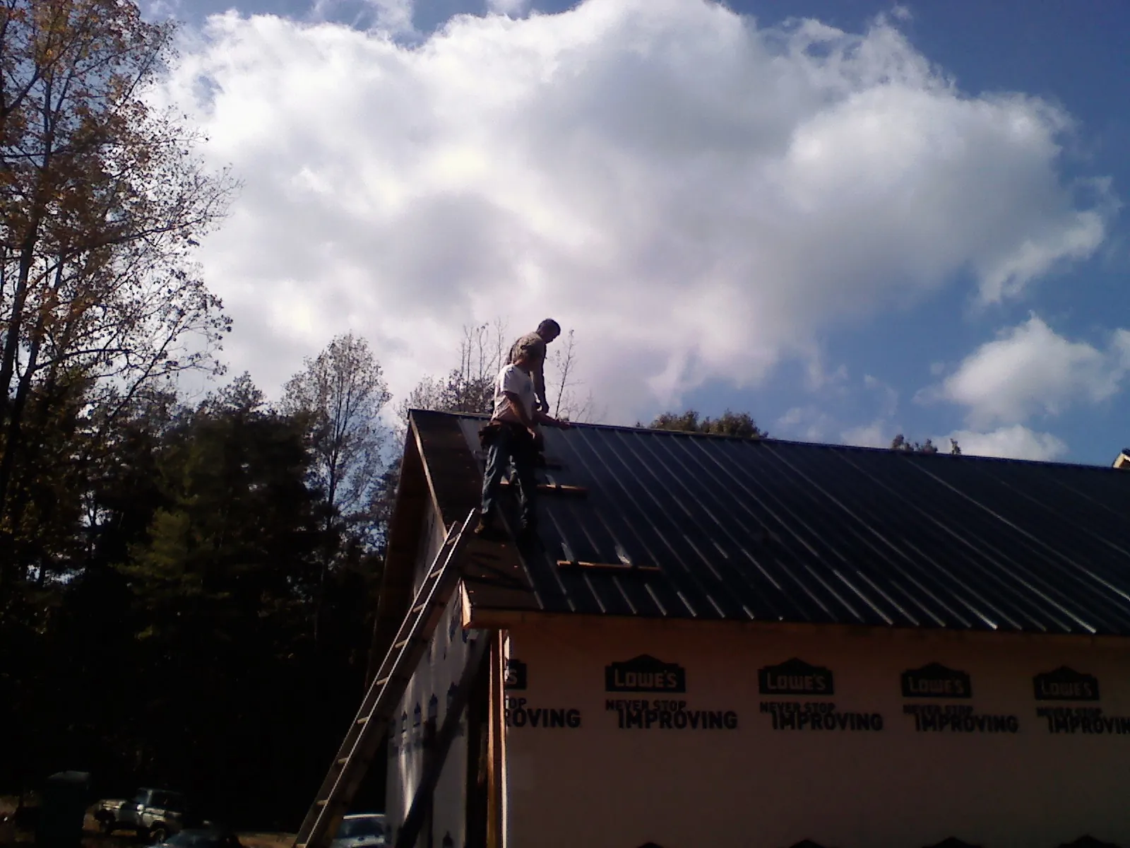 Roofer fastening dark metal panels high against a cloudy sky, from a Roof Inspection job in Glasco