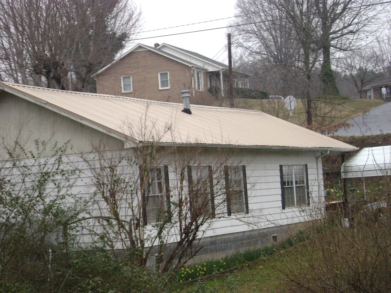 Tan metal roof on a white sided house set into a hillside — Commercial Roofing by Roofing Brothers in Glasco