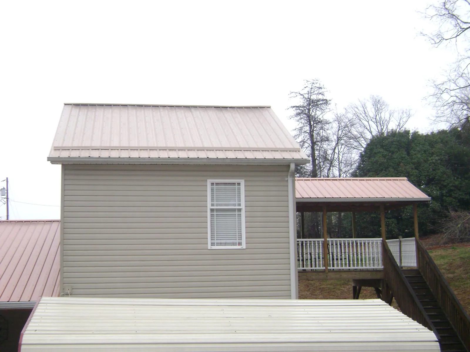 Tan metal roofs on a two story addition and attached porch, from a Roof Replacement job in Glasco
